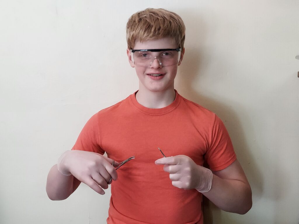 A teen or tween who wants to be a doctor and is holding dissection instruments and wearing safety goggles