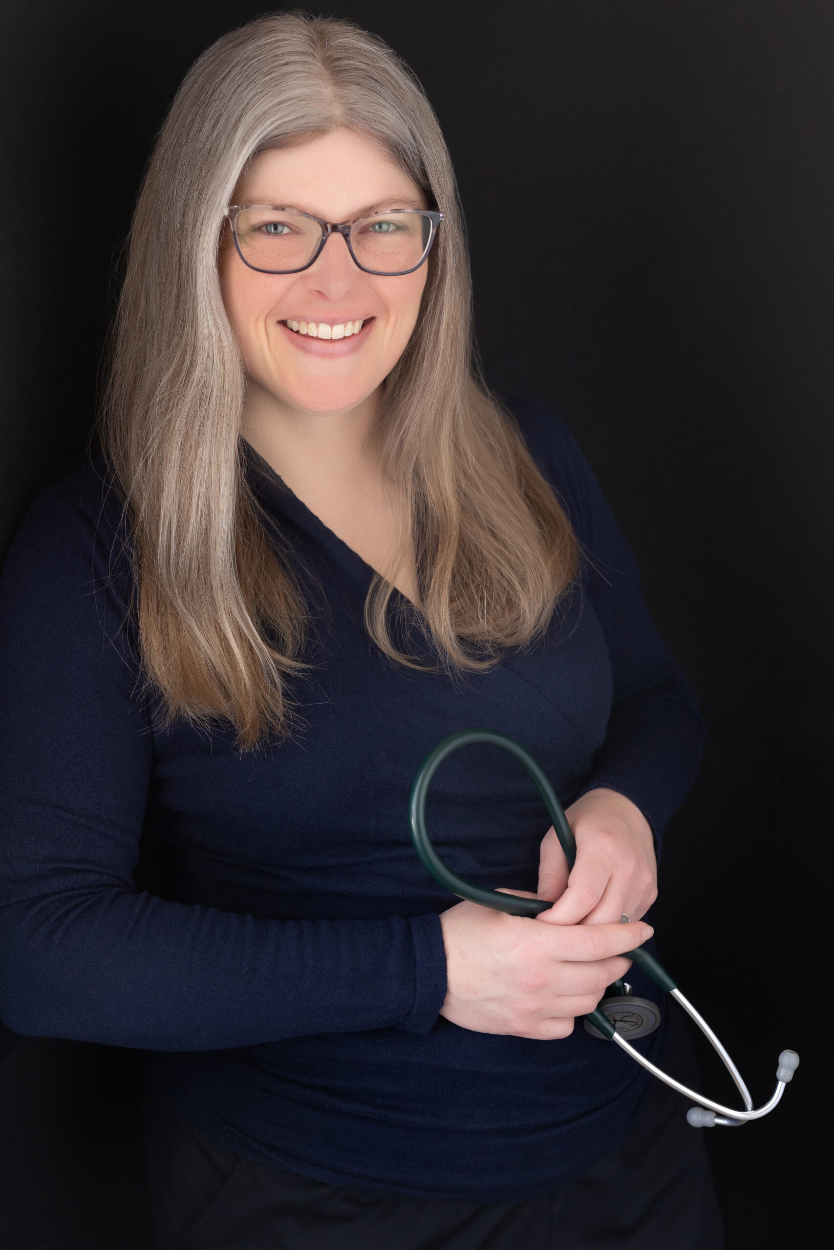 Dr. Robin, a successful female physician, holding her stethoscope and learning against a wall