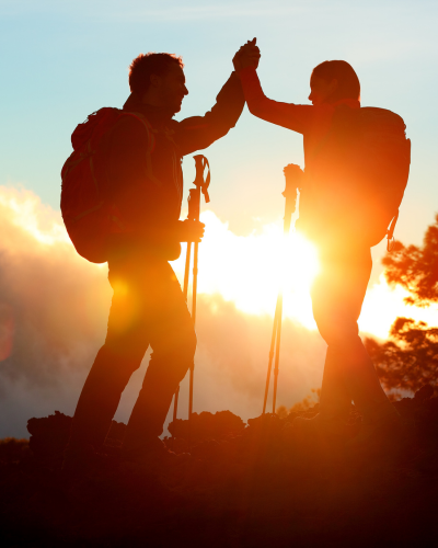 two people rejoicing when they reach the summit, sun peaking through clouds
