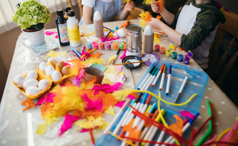 a kids craft table covered with markers and glue and feathers and eggs (??)